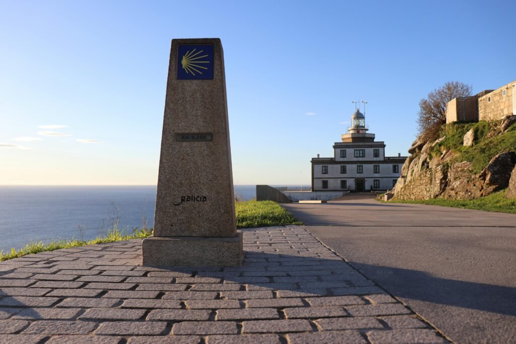 Cabo Fisterra lighthouse under clear blue sky in Galicia, Spain with kilometer zero landmark.