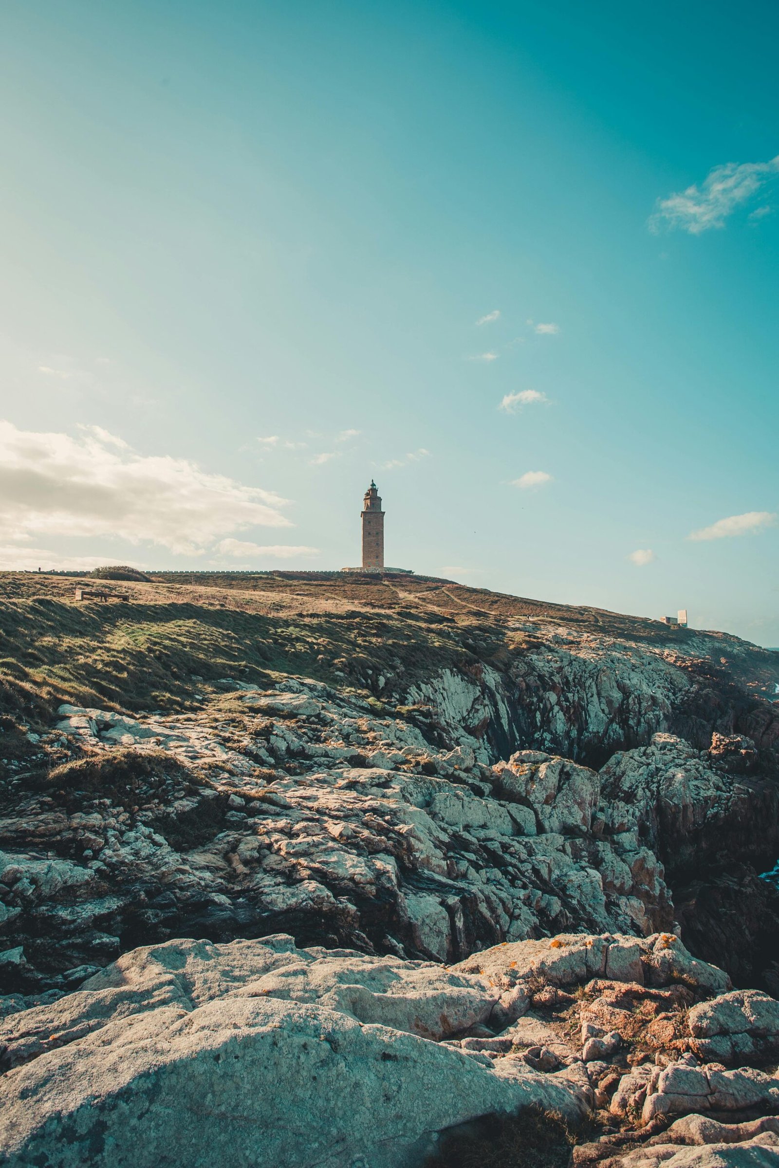 Lighthouse standing tall on rocky cliff with clear blue sky, ideal for nature and travel themes.