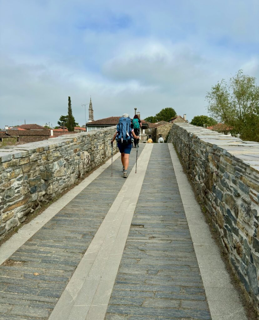 Two hikers with backpacks walking on an ancient stone pathway under a cloudy sky.