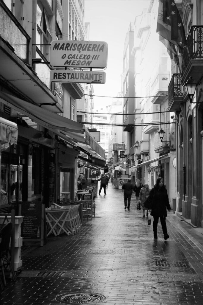 A grayscale photo of people walking in an atmospheric alley in A Coruña, Spain.