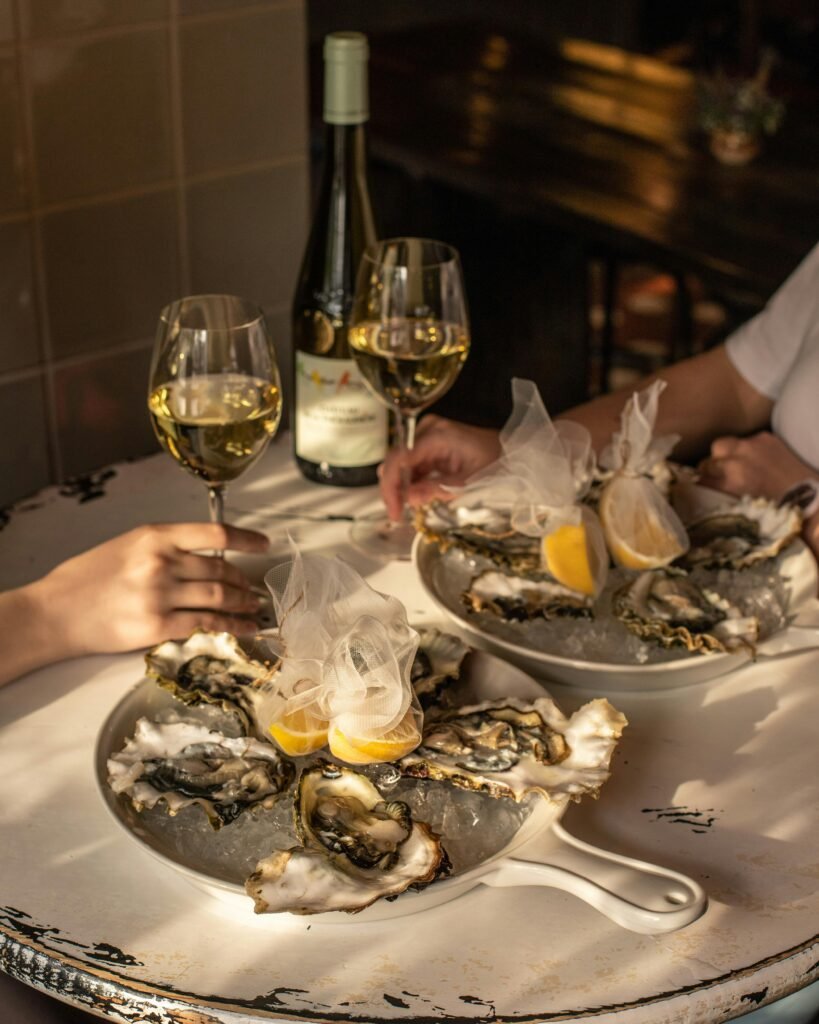 Crop romantic couple having dinner in restaurant drinking white wine and eating oysters with lemon juice