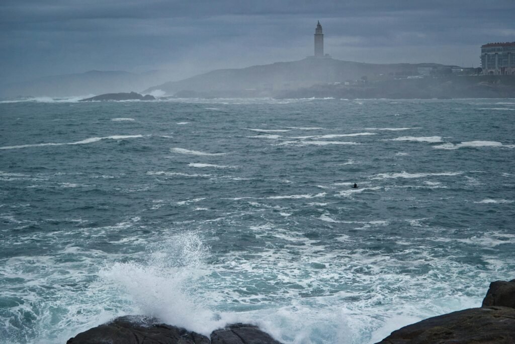 Waves crash against the rocky coast of A Coruña with the historic Tower of Hercules in the background.