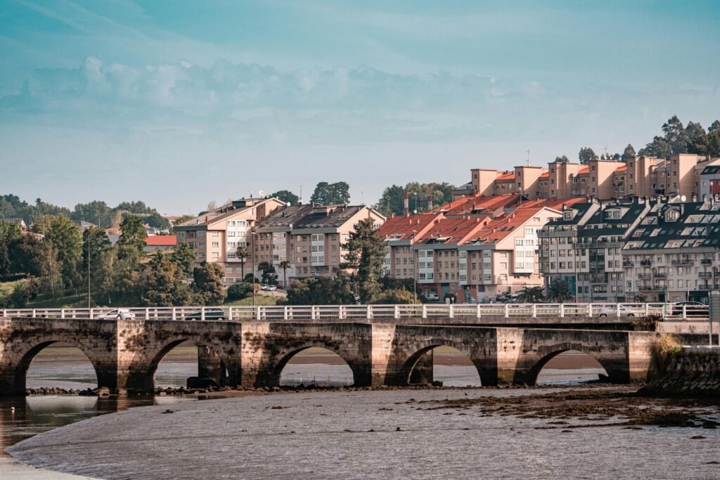 Picturesque view of a historic bridge and vibrant buildings in Cambre, Galicia, Spain under a clear blue sky.