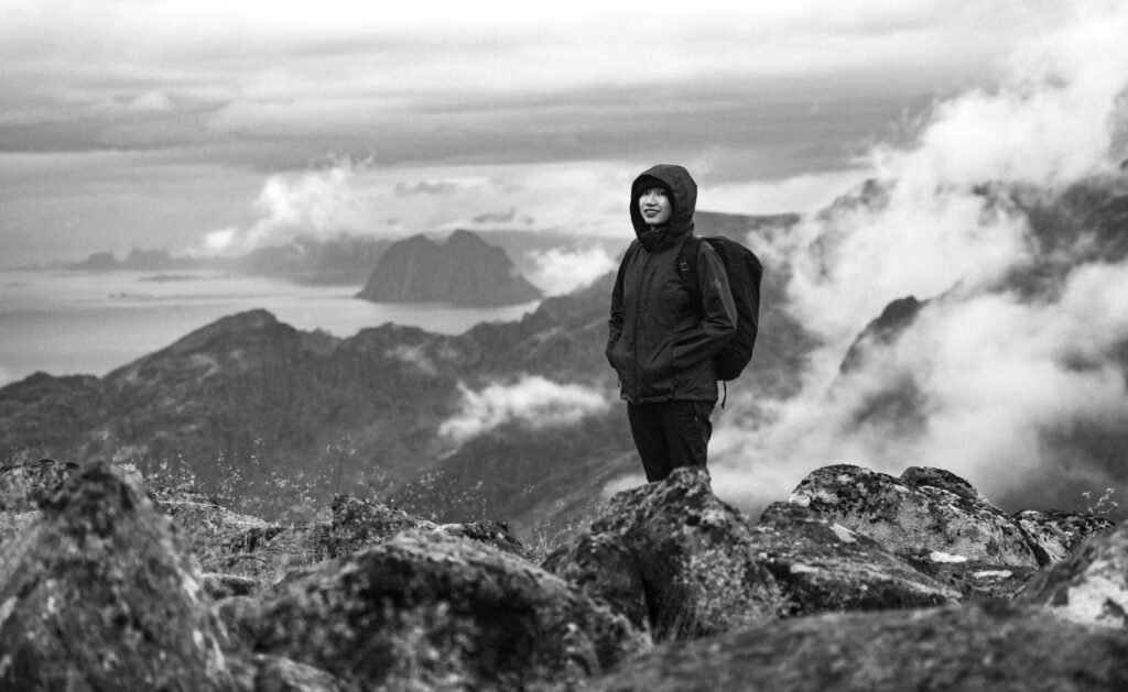 A solitary hiker stands amidst the dramatic mountains of Nordland, Norway, shrouded in clouds.