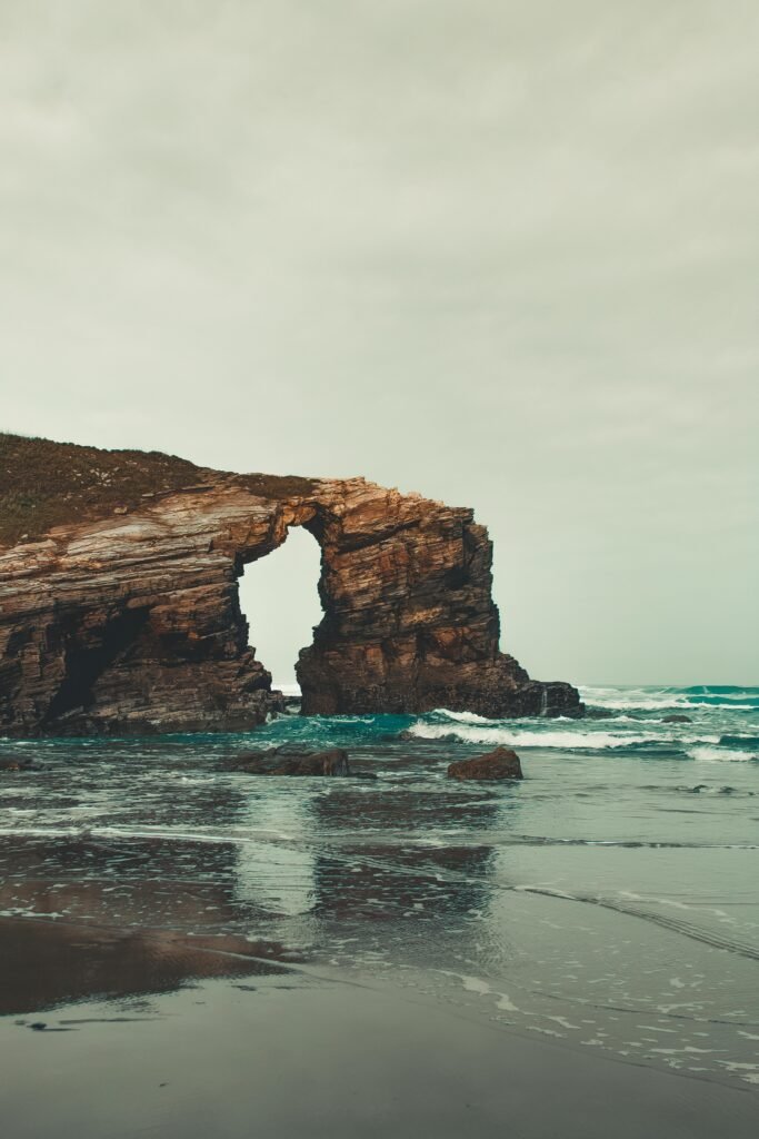 Capture of a stunning beach featuring a natural rock arch with waves gently lapping at the shore.