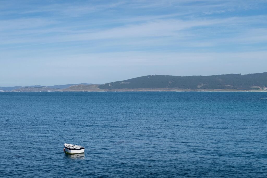 A single white boat floats on serene blue ocean waters under a clear sky.