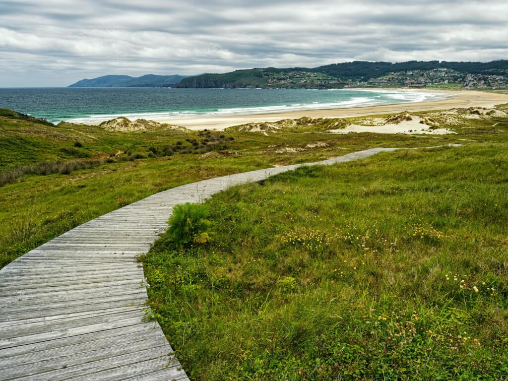 Beautiful seaside landscape with a wooden boardwalk leading to a sandy beach in Galicia, Spain.